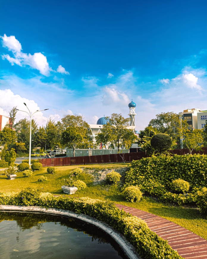 Lush green Central Park in Hulhumalé, Maldives, with winding walkways through tropical gardens, modern benches under palm trees, and the city skyline in the background