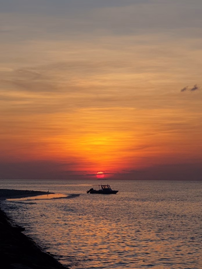 Golden sunset over Keyodhoo Island's calm ocean in Vaavu Atoll, Maldives, with silhouetted fishing boats on the horizon