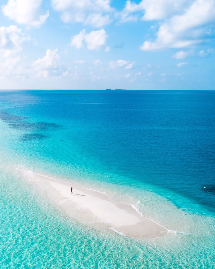 A guest walking barefoot on Rasdhoo's secluded sandbank at low tide, surrounded by crystal-clear turquoise waters in North Ari Atoll, Maldives